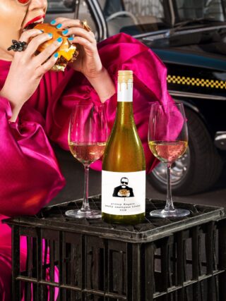 Greasy Food: Woman taking a bite of a burger with a bottle of white wine in front of her